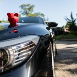 Rotes Sparschwein platziert auf der Motorhaube eines Luxusautos