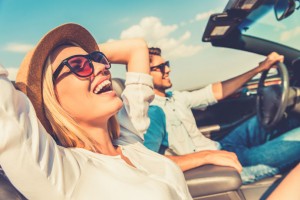 Junges Paar genießt die Fahrt in einem offenen Cabrio bei Sonnenschein